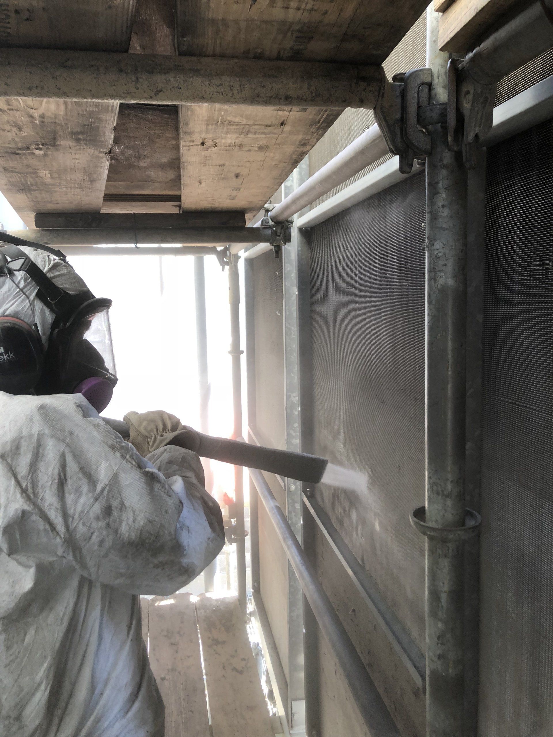 A man wearing a helmet and goggles is spraying a wall with a hose.