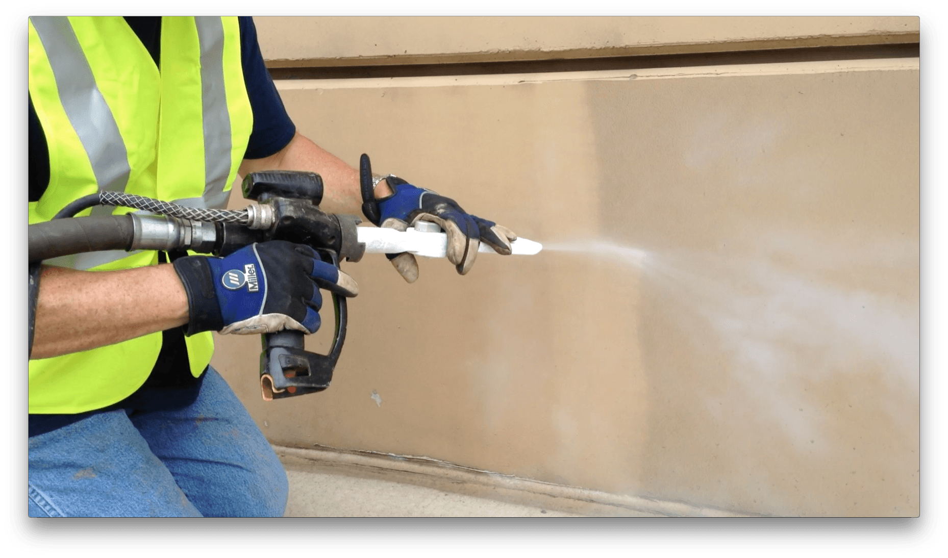 A man wearing a yellow vest and blue gloves is spraying something