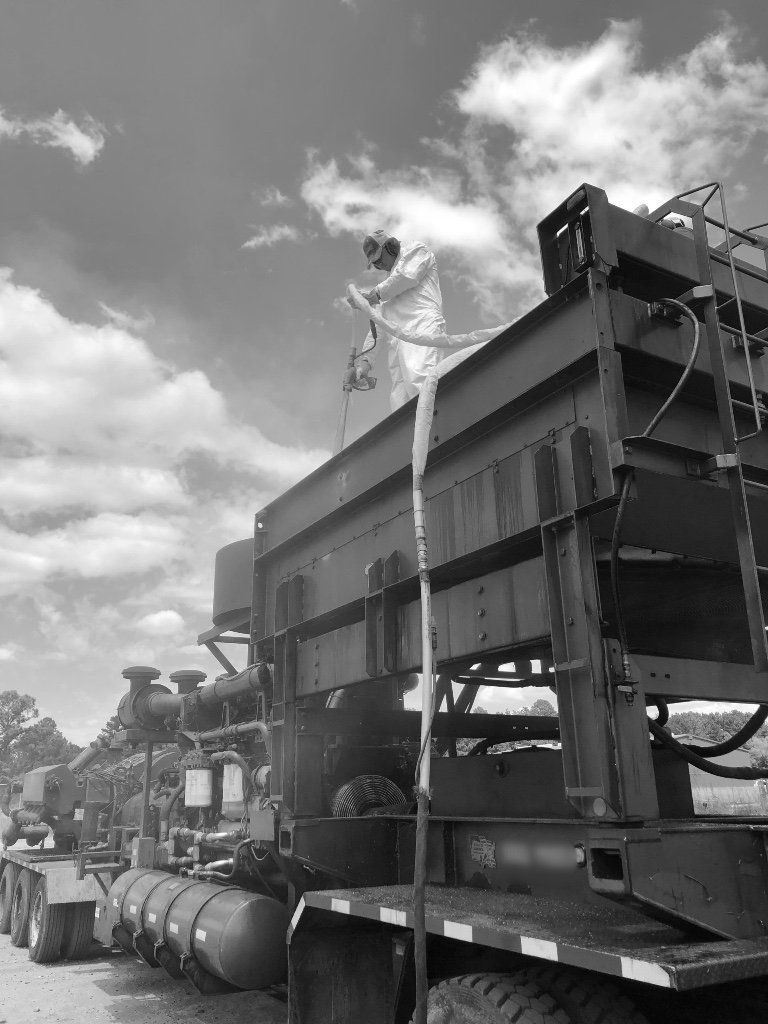 A black and white photo of a man spraying a truck with a sprayer.