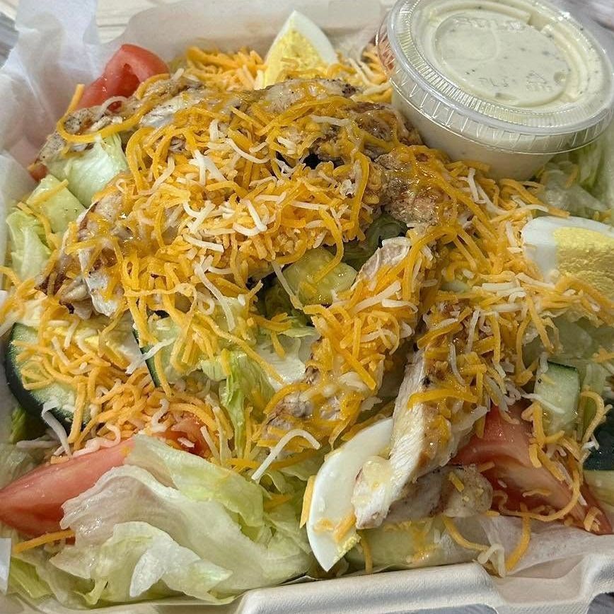A salad with lettuce , tomatoes , cucumbers , eggs and cheese in a styrofoam container.