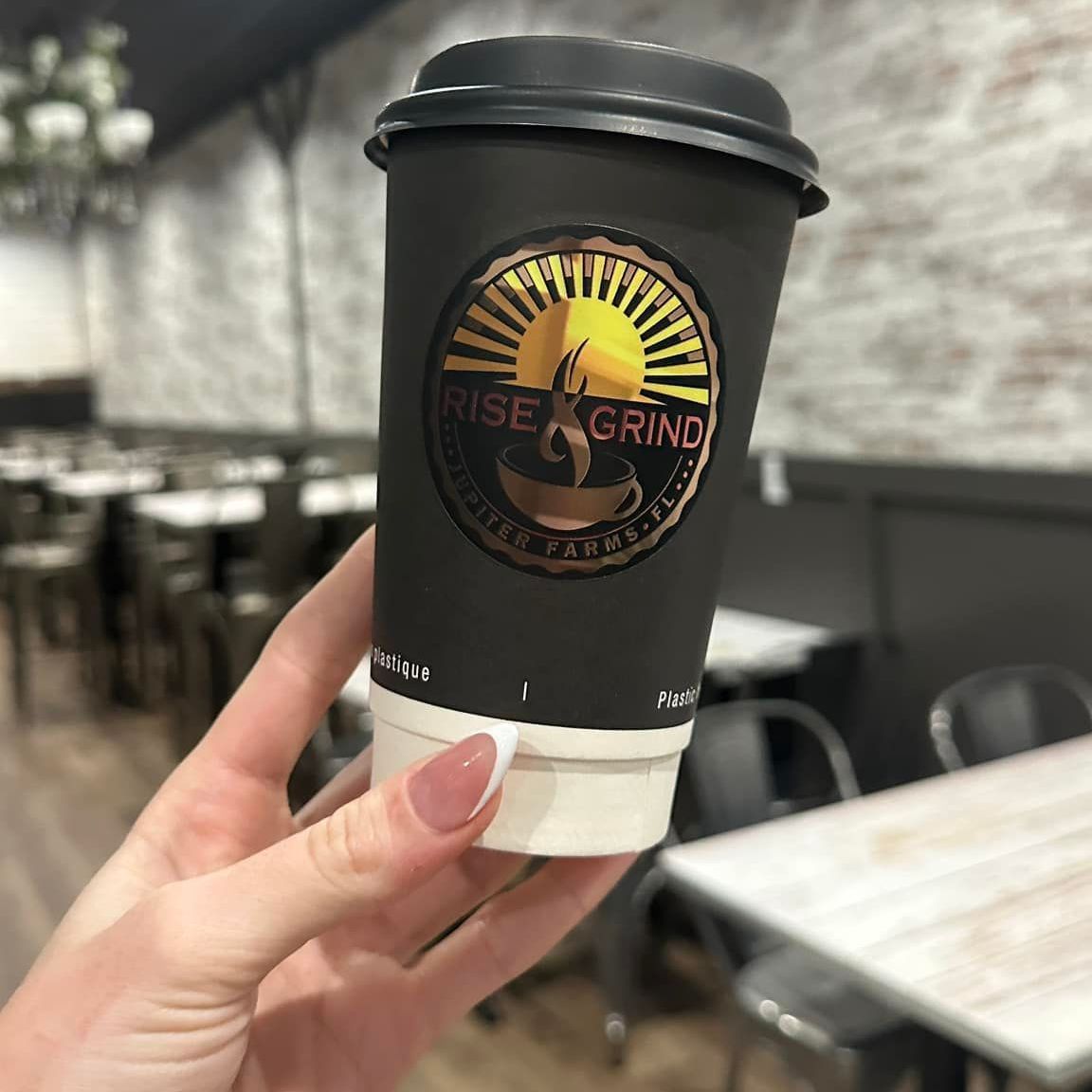 A person is holding a cup of coffee that says rise grind