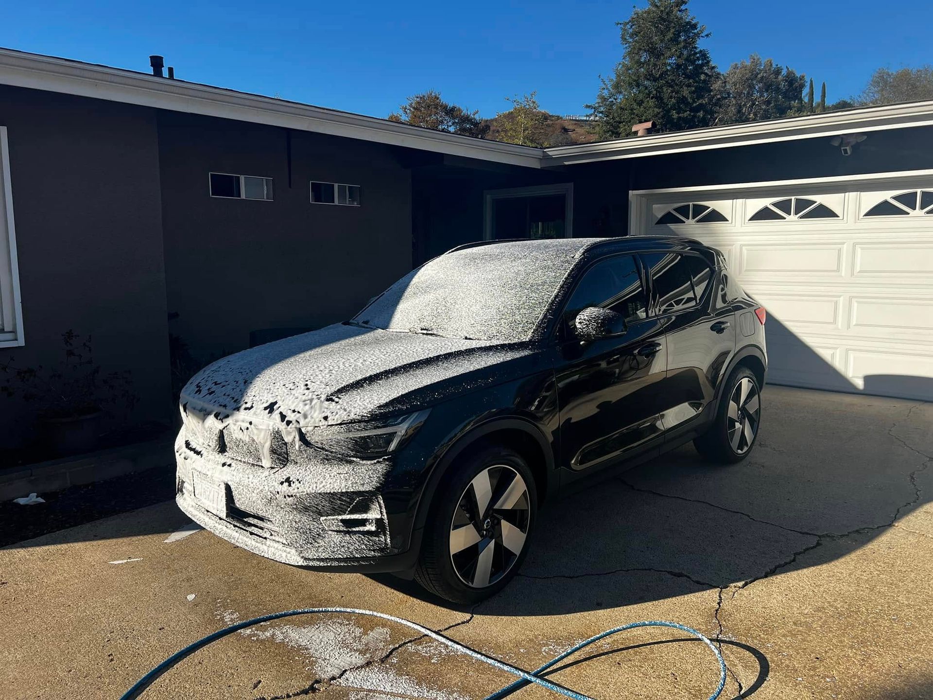 A black car is covered in foam in front of a garage.