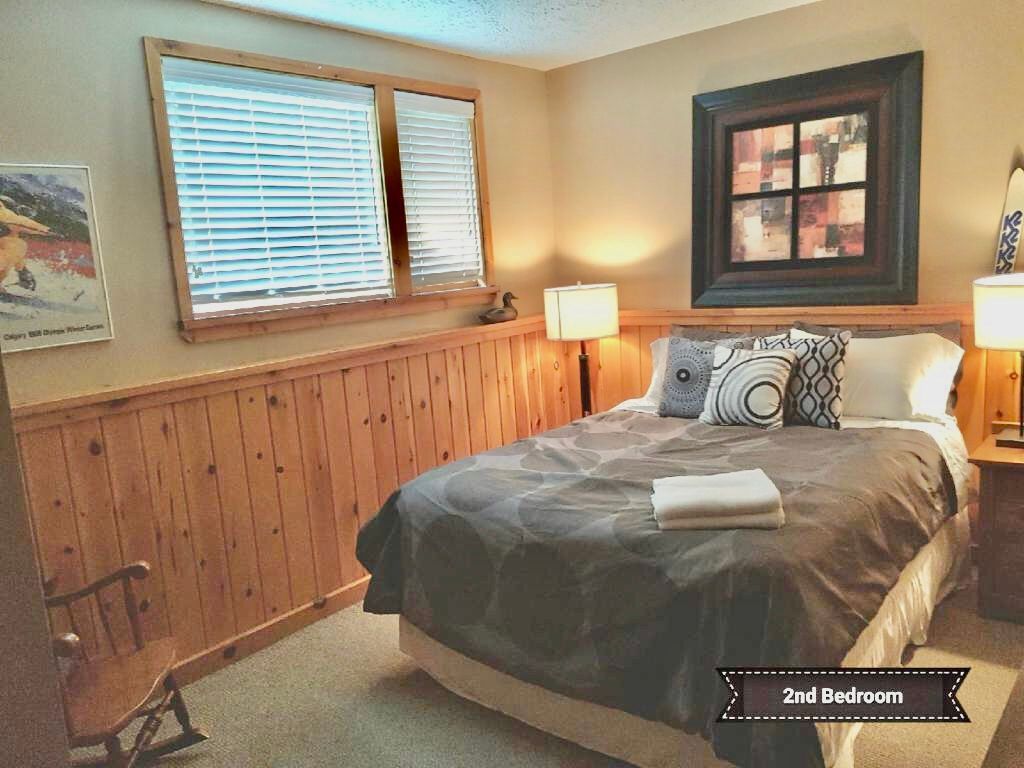 A bedroom with a bed , two windows and a rocking chair.