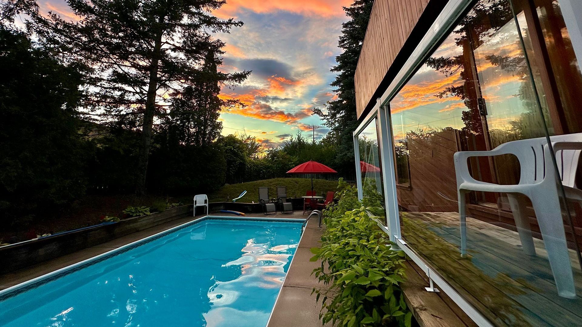 A large swimming pool is surrounded by chairs and trees at sunset.
