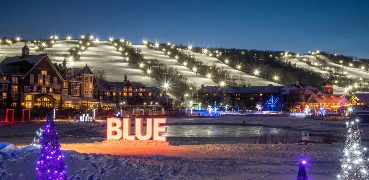 A ski resort is lit up at night with a blue sign in the foreground.
