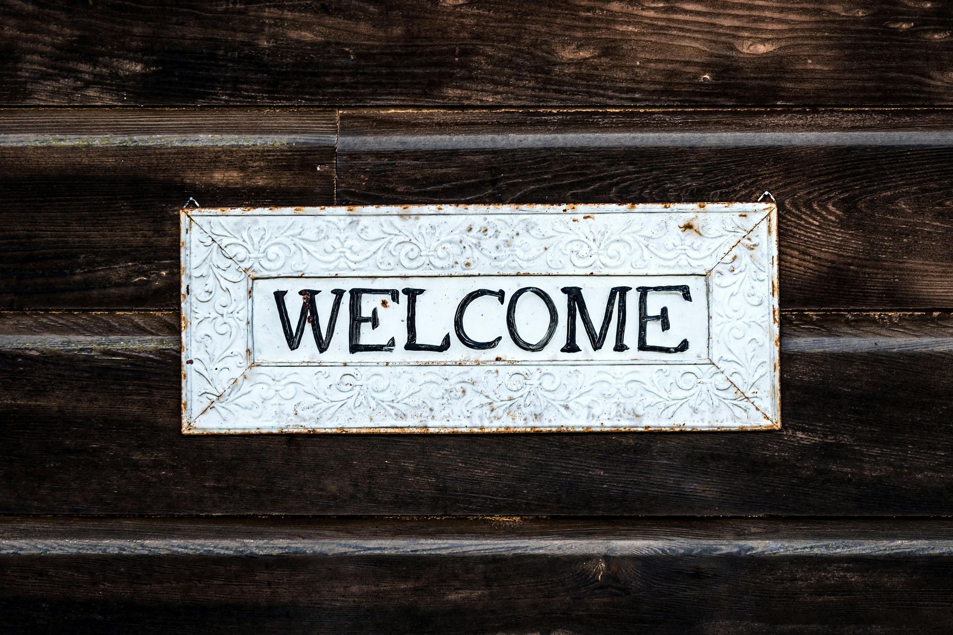 A white welcome sign is hanging on a wooden wall.
