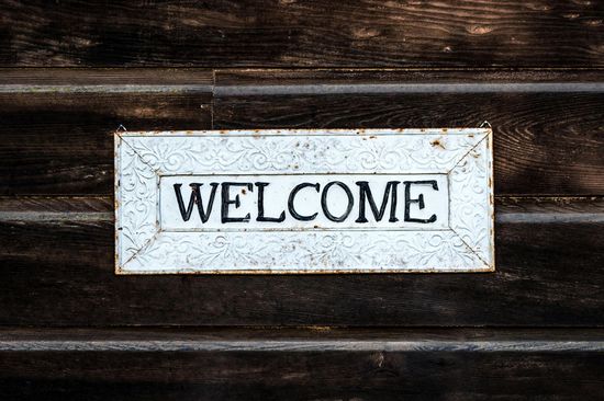 A white welcome sign is hanging on a wooden wall.