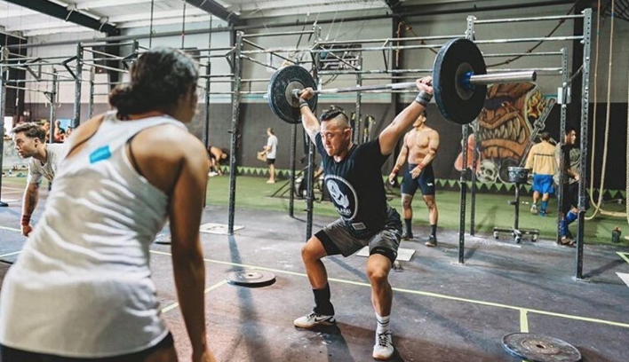 A man is squatting down with a barbell over his head in a gym.