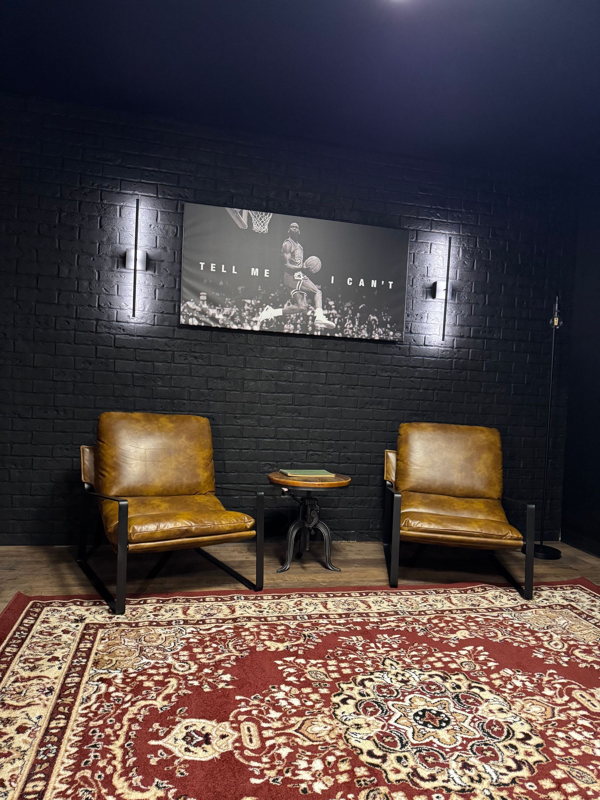 A room with two chairs , a rug and a painting on the wall.