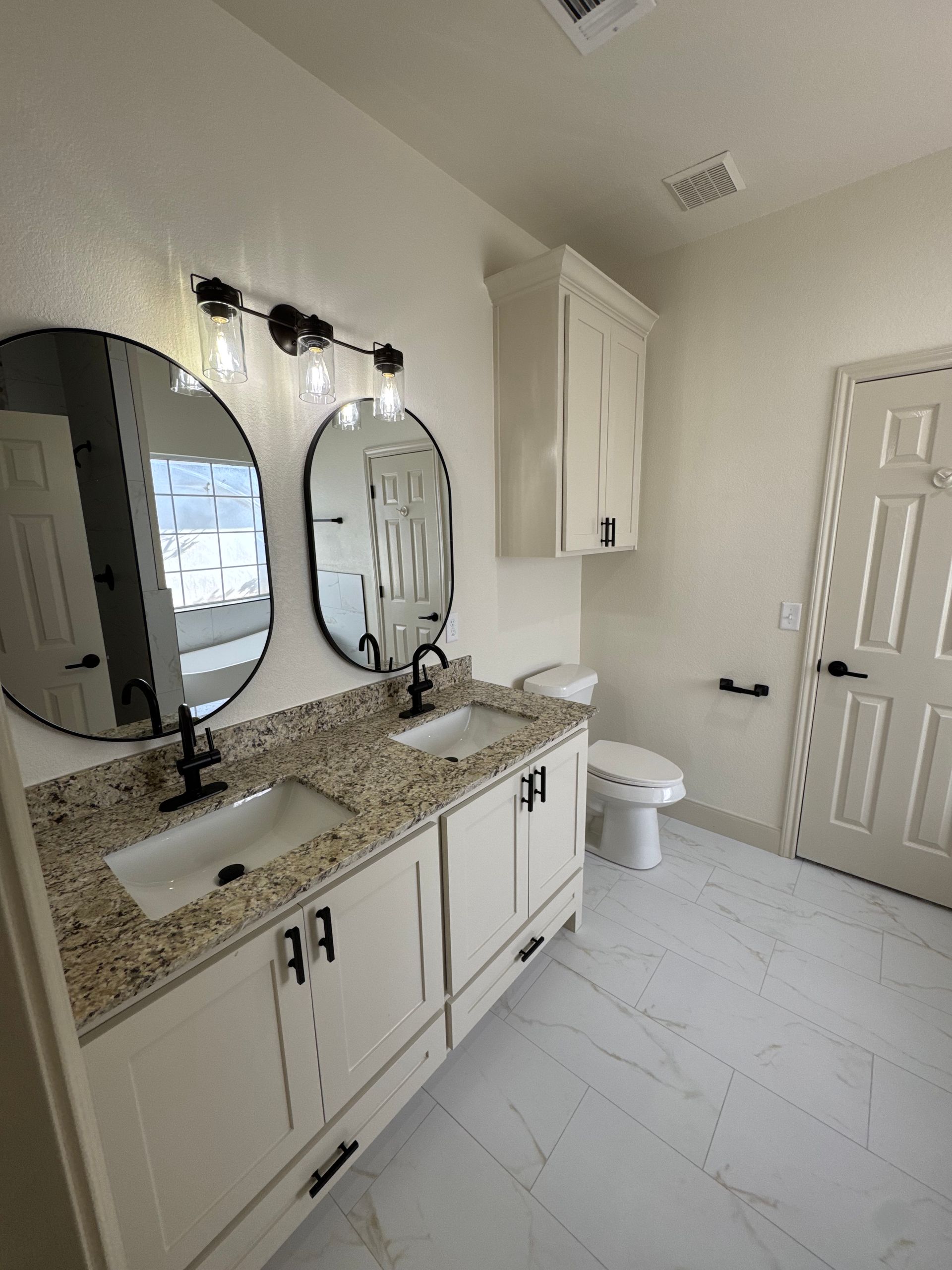 A bathroom with two sinks , a toilet , and two mirrors.