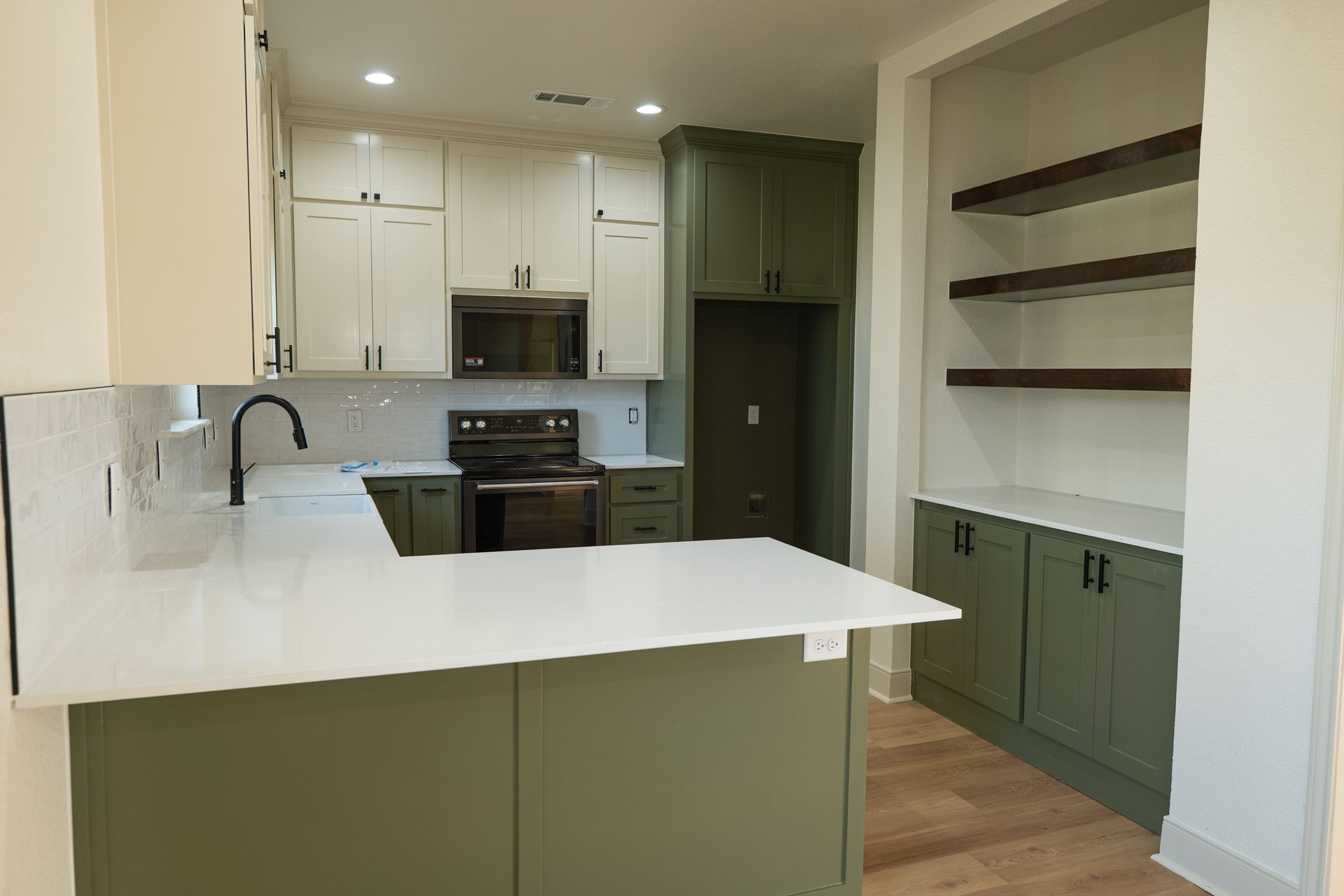A kitchen with green cabinets , white counter tops , and a stove.