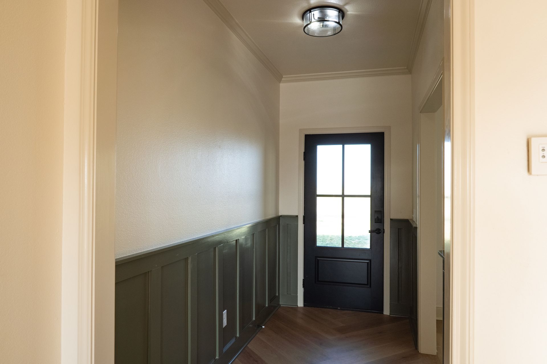 A hallway with a black door and a light on the ceiling.