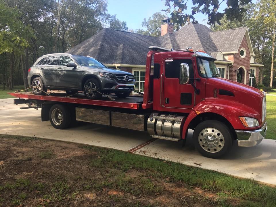 A red tow truck with a car on the back is parked in front of a house.