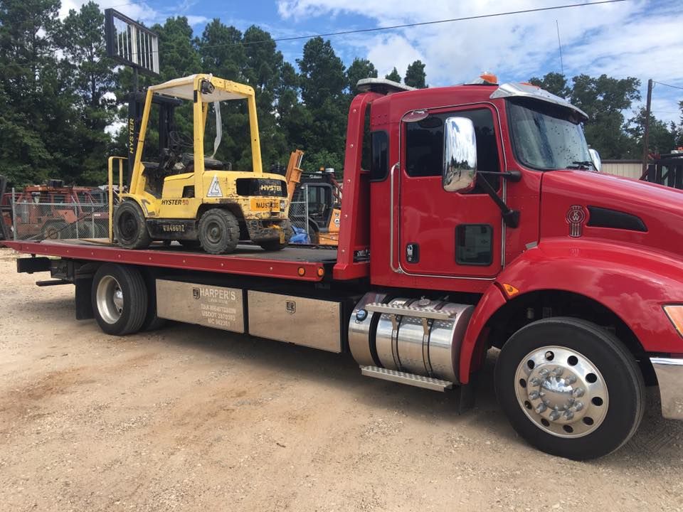 A red tow truck with a yellow forklift on the back of it.