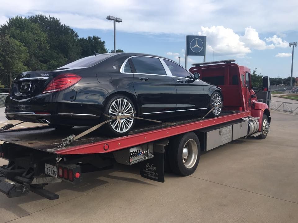 A black mercedes benz is being towed by a tow truck.
