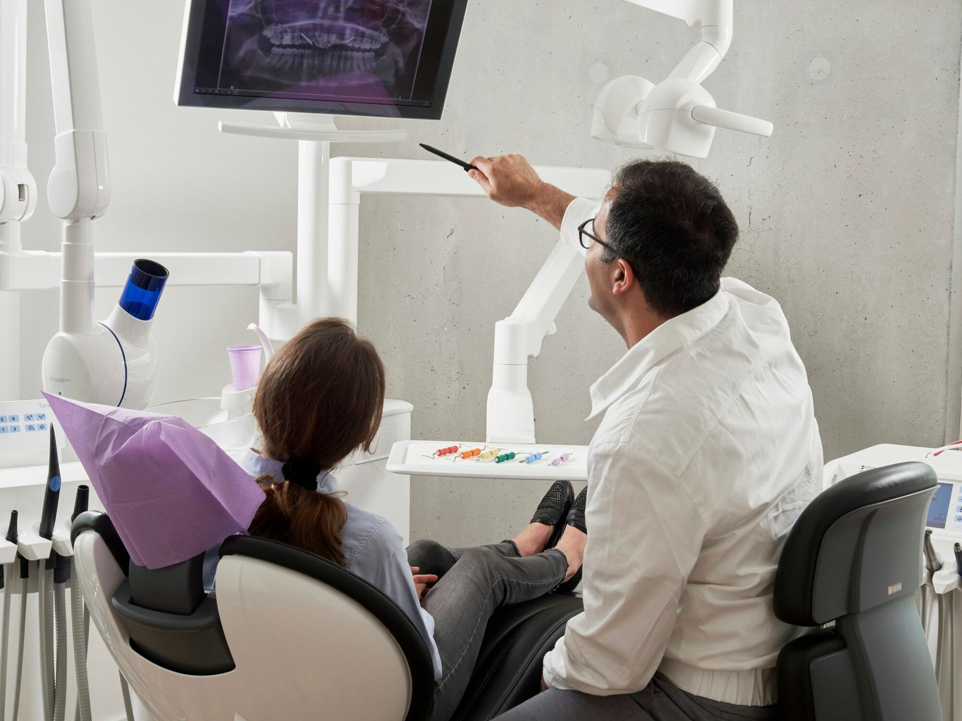a woman sits in a dental chair looking at an x-ray of her teeth