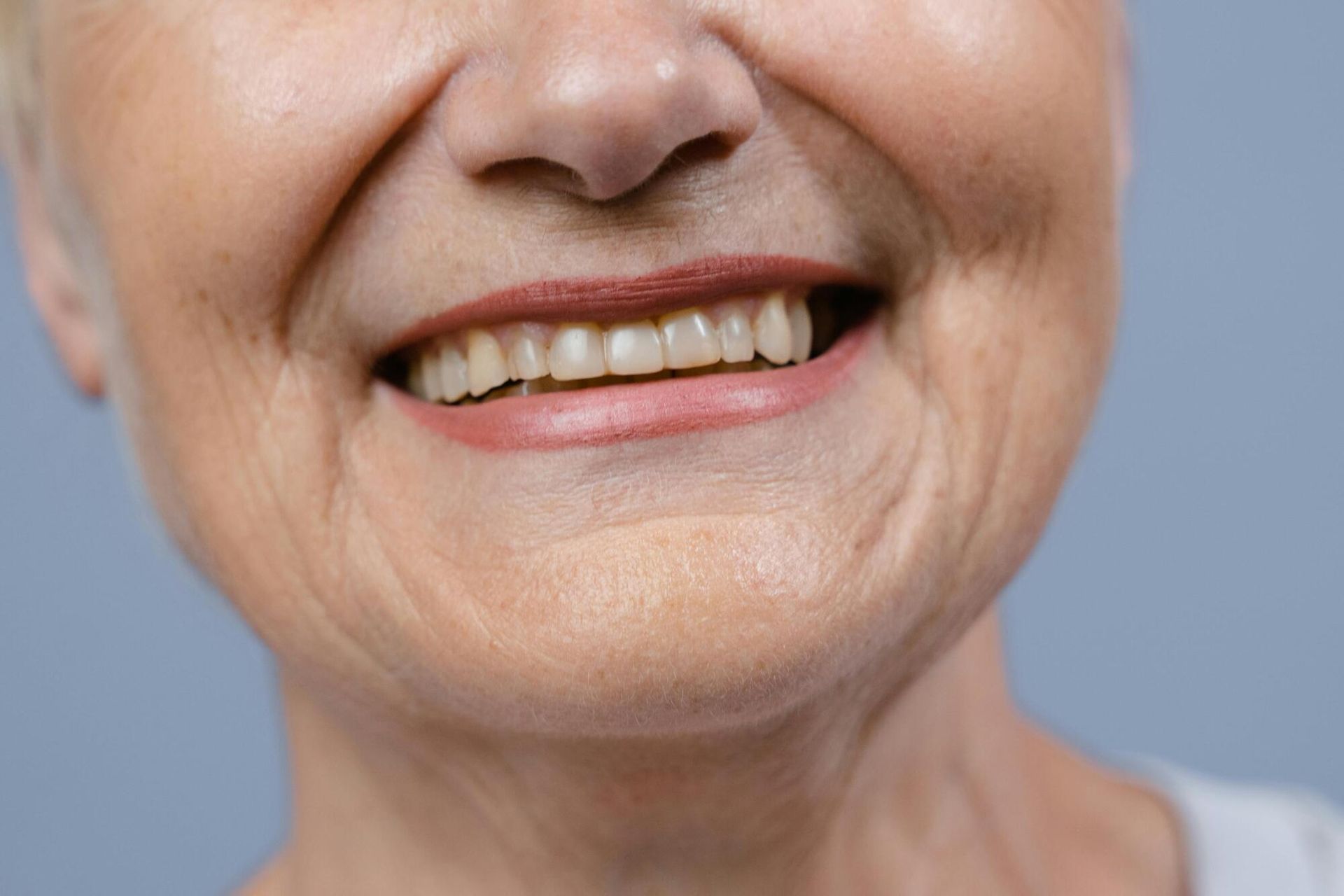 A close up of an elderly woman 's smile with a gray background.