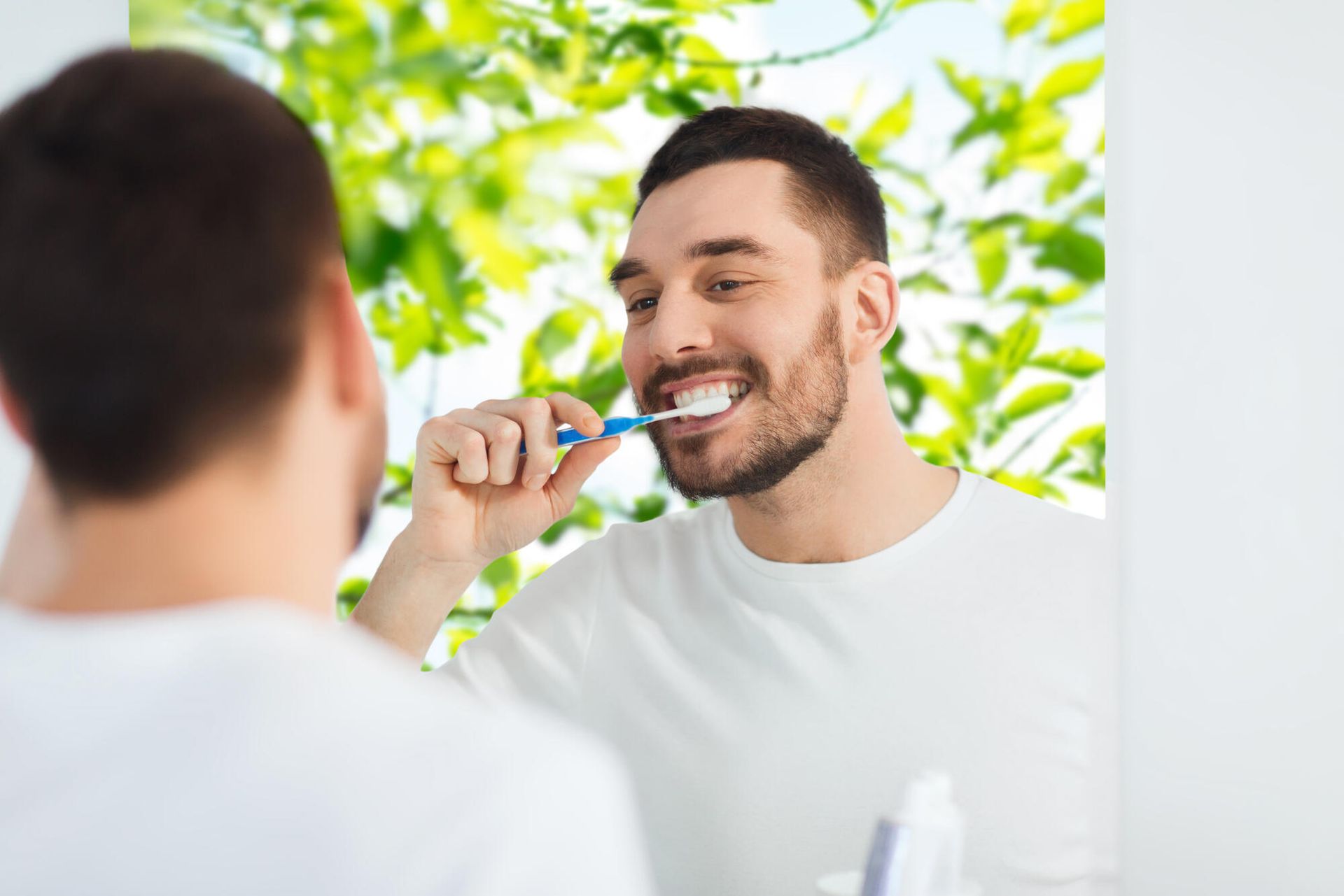 A man is brushing his teeth in front of a mirror.