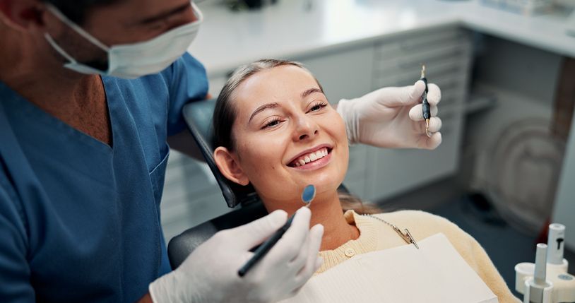 Dentist examining a smiling patient with tools in a bright clinic