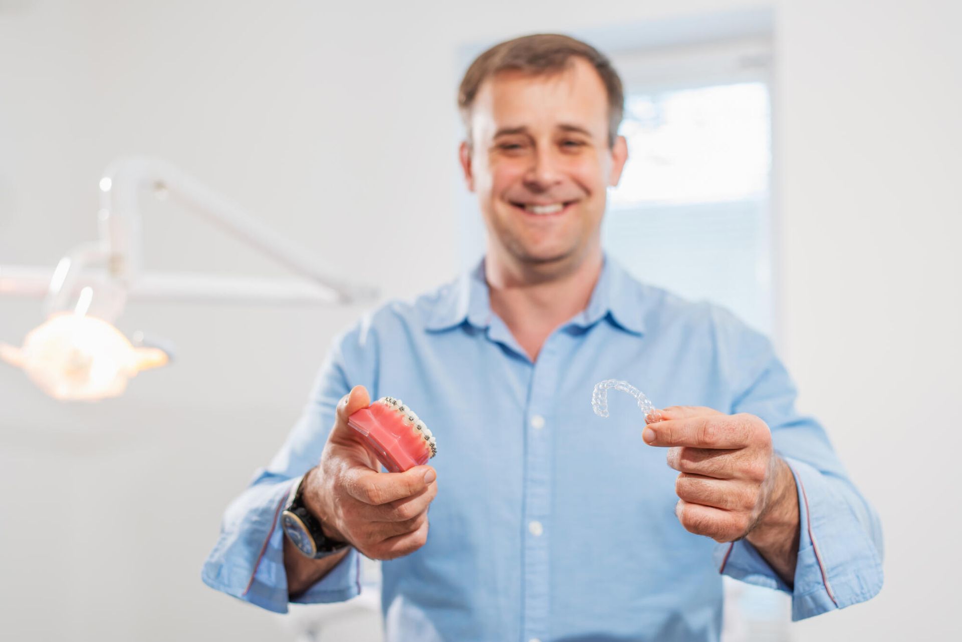 A man is holding a denture and a retainer in his hands.