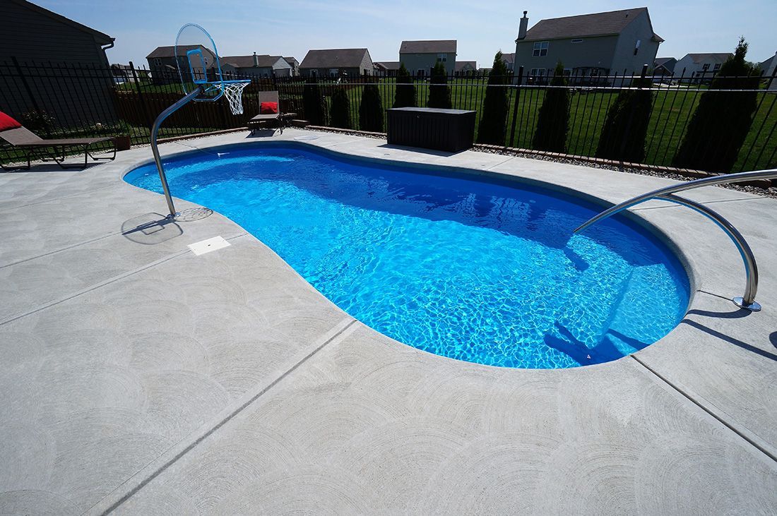 Blue-tiled backyard swimming pool with a basketball hoop, surrounded by concrete and landscaping.