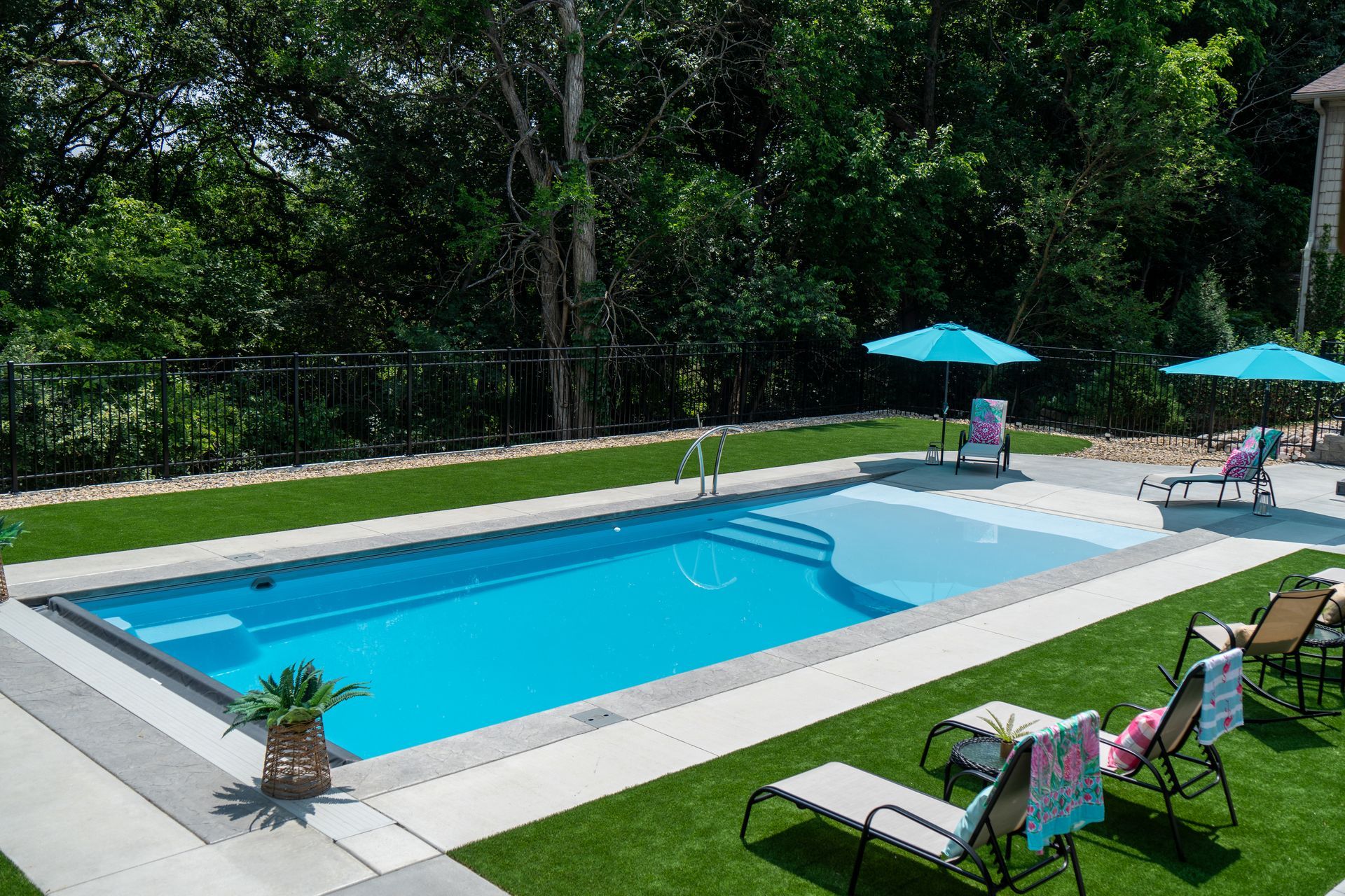 A large swimming pool surrounded by chairs and umbrellas in a backyard.