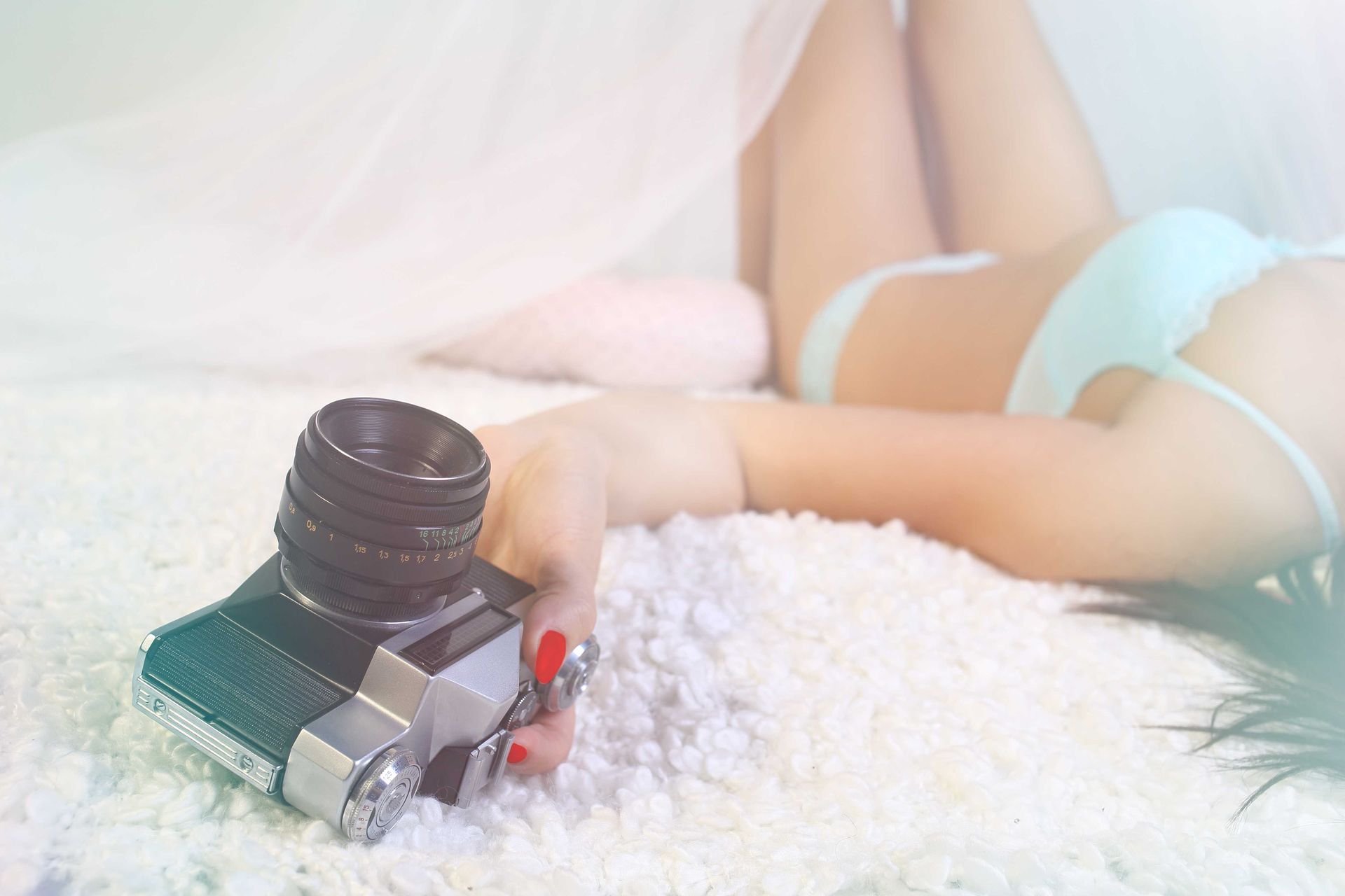 A woman lying on her back with a professional camera in her hand for a boudoir shoot