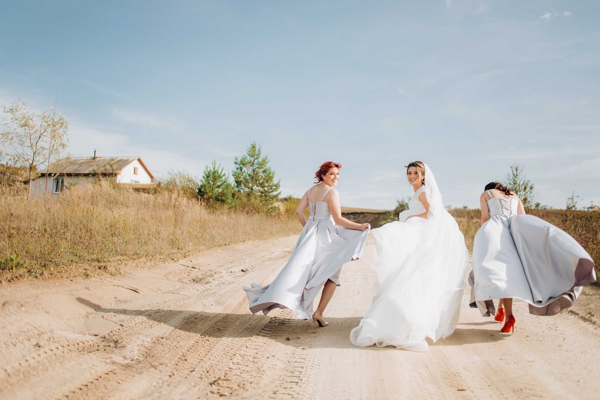 Bride and bridesmaids running down dirt road for photoshoot