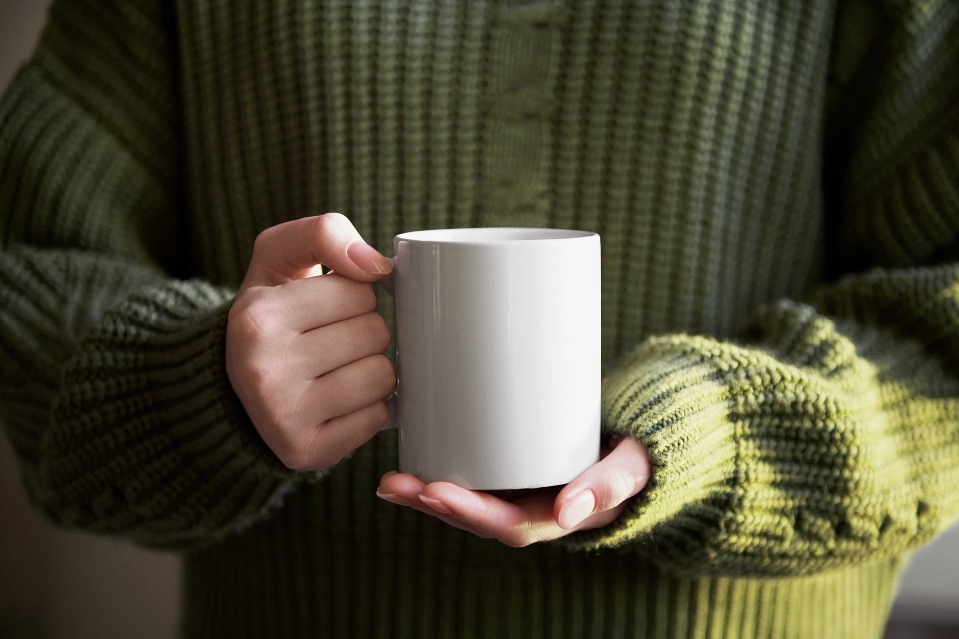 Marketing photo of a person holding a white coffee mug out in front of them
