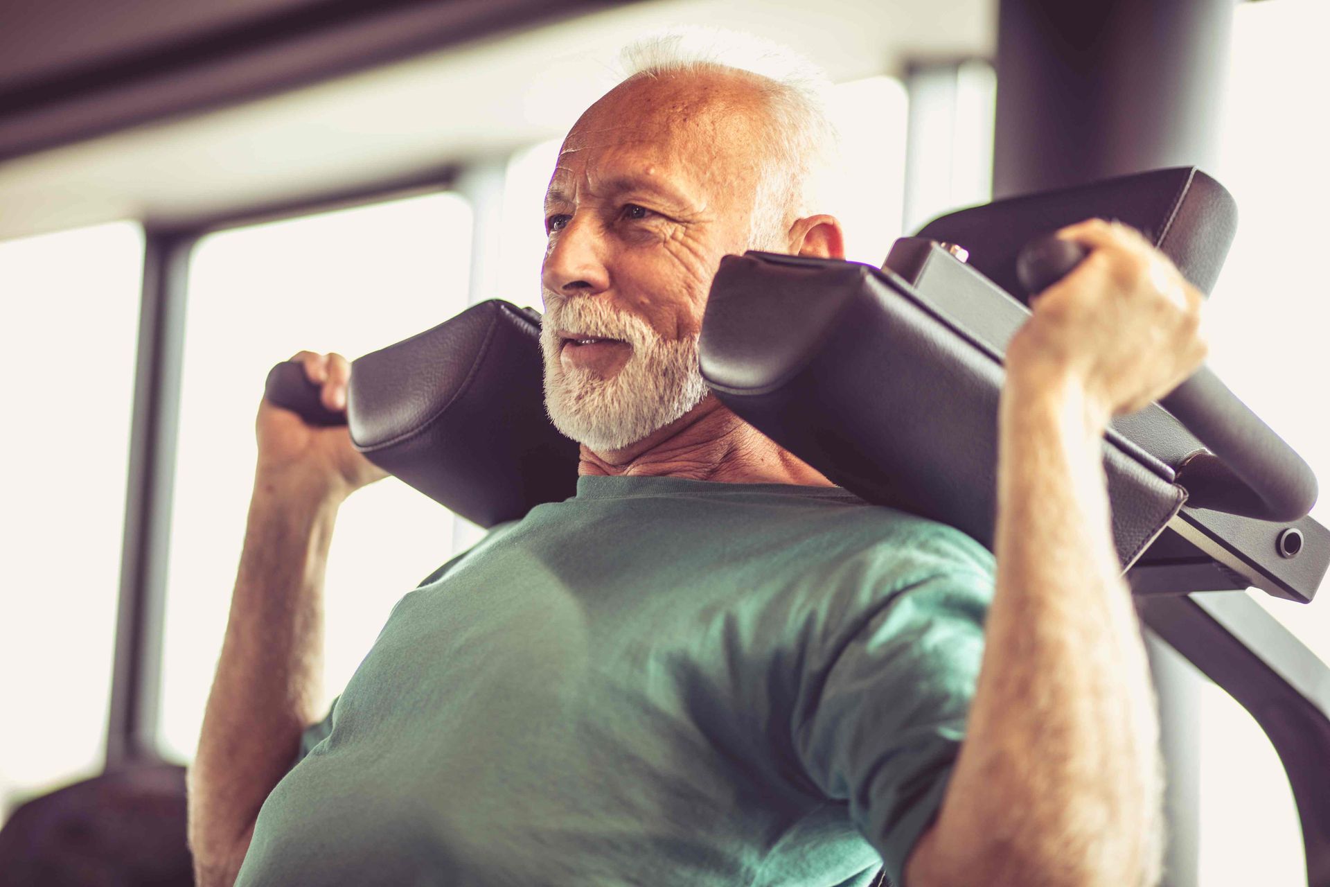 A photo of an elderly man doing shoulder presses on a machine