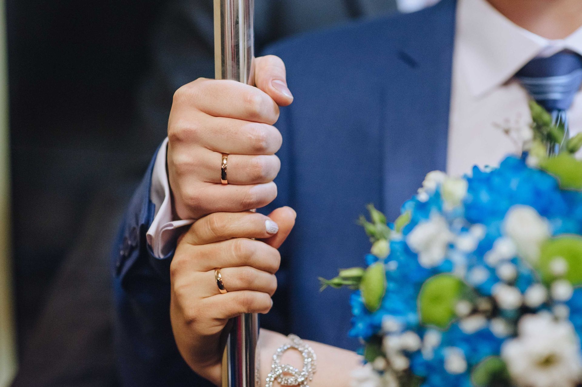A couple with wedding bands holding on to a pole with hands