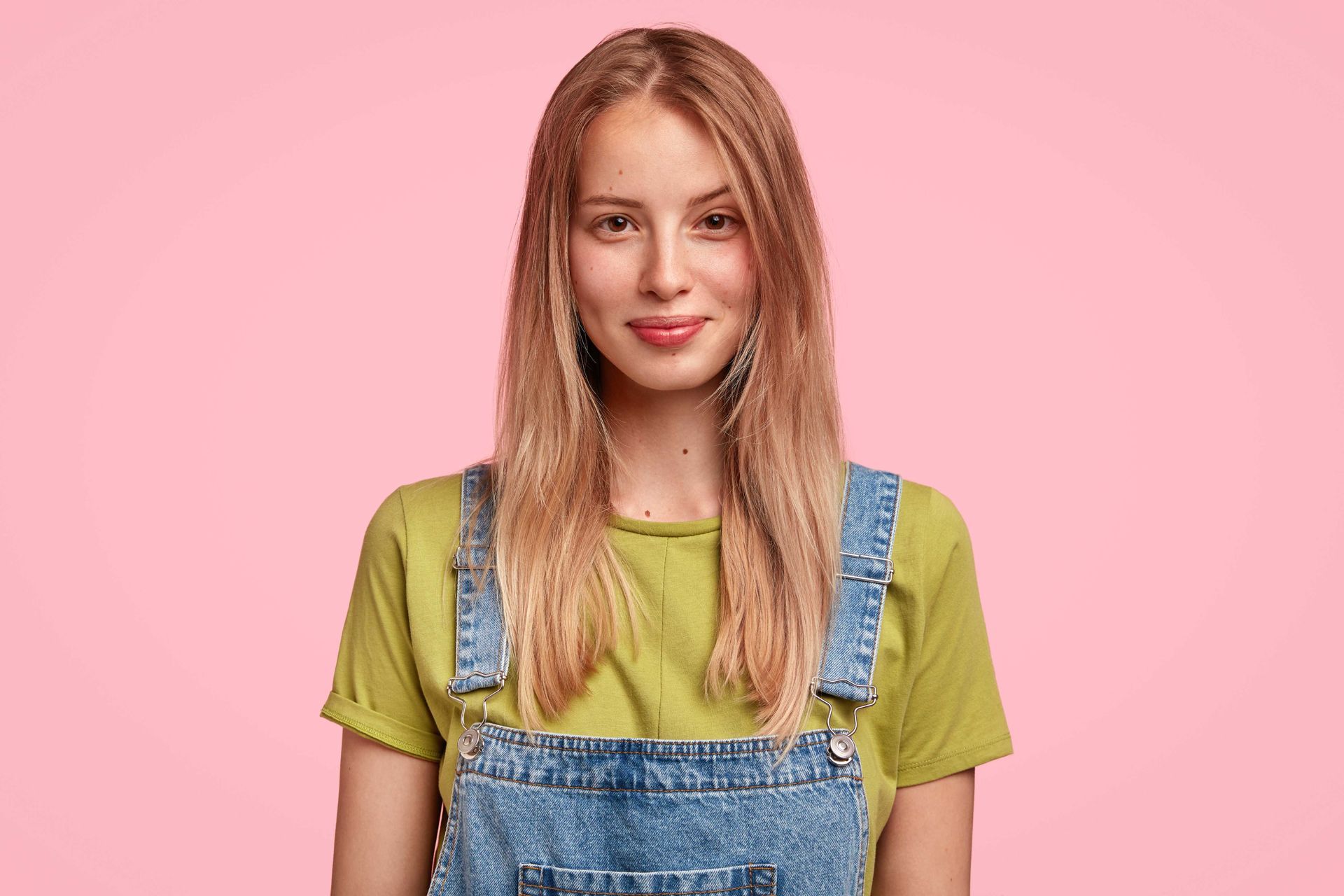 A Texas woman with jean overalls over top of a pastel green t-shirt