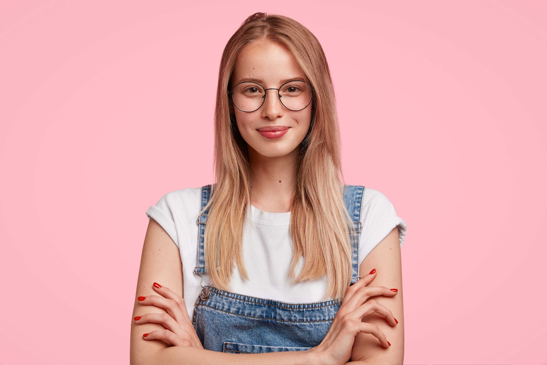 A pretty Texas woman with glasses and jean overalls over a white t-shirt