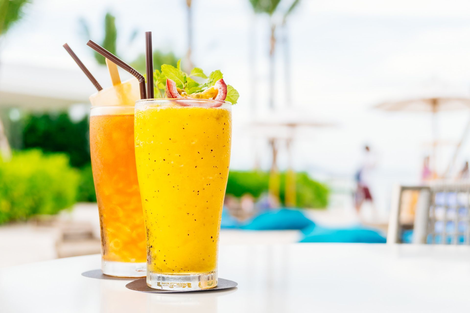 Two glasses of orange juice with straws on a table.