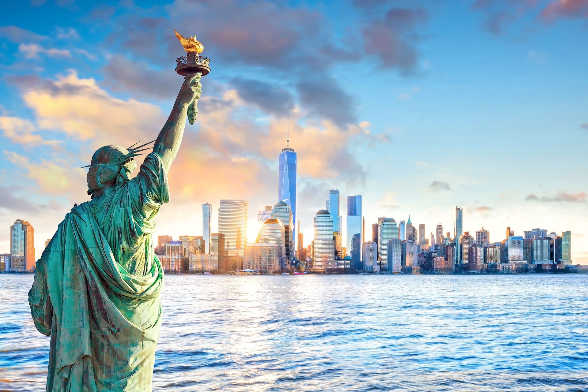The statue of liberty is standing in front of the new york city skyline.
