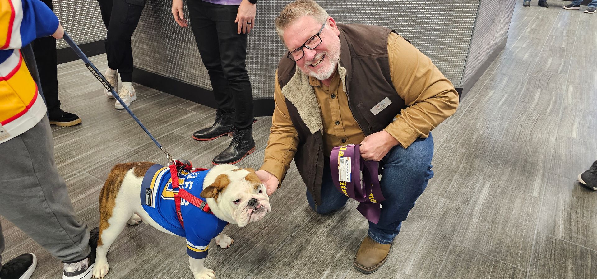 A man is kneeling down next to a bulldog on a leash.