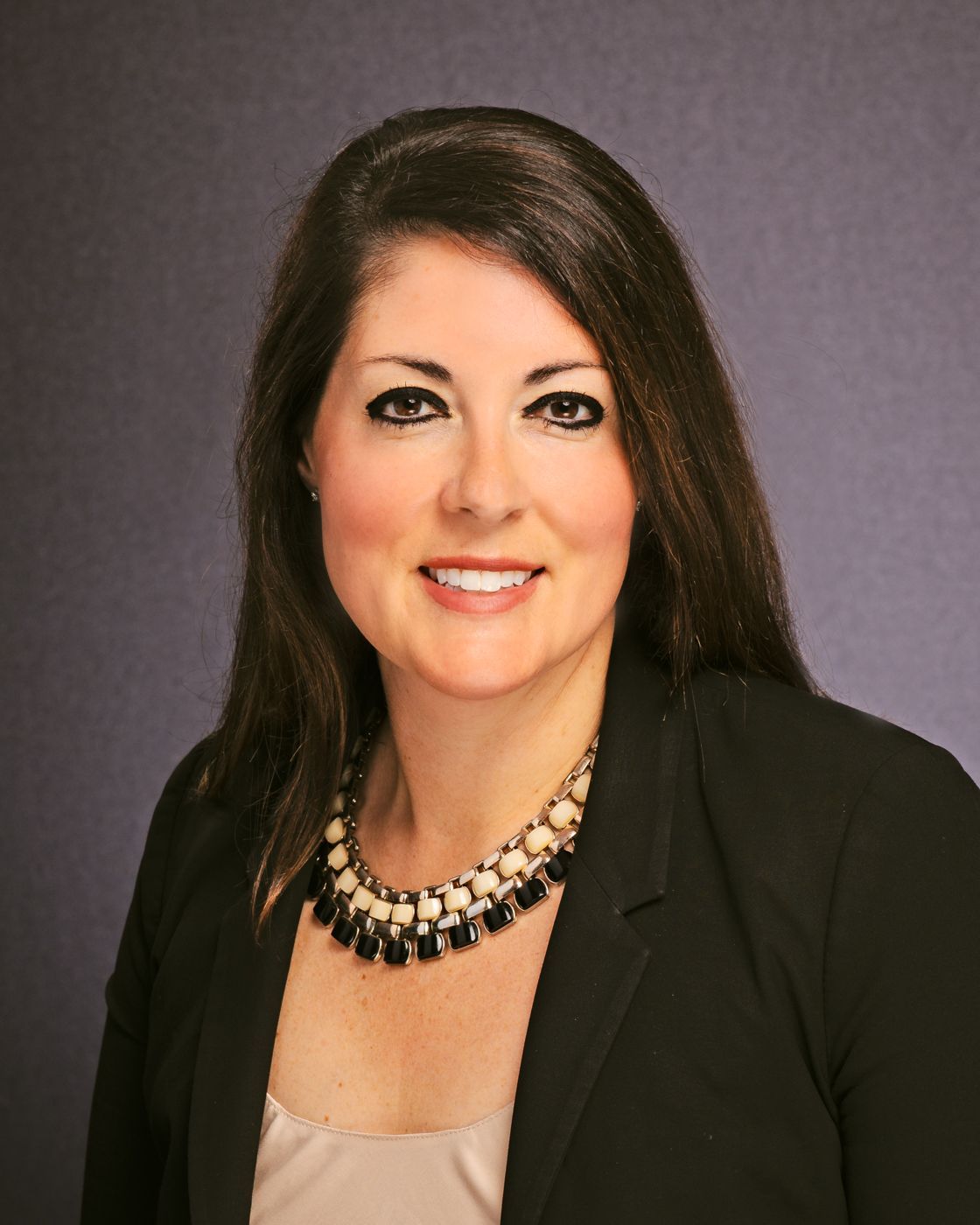 A woman wearing a black jacket and a necklace is smiling for the camera.