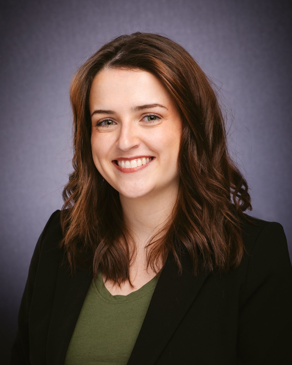 A woman in a black jacket and green shirt is smiling for the camera.