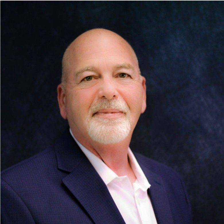 A bald man with a beard is wearing a blue suit and white shirt.