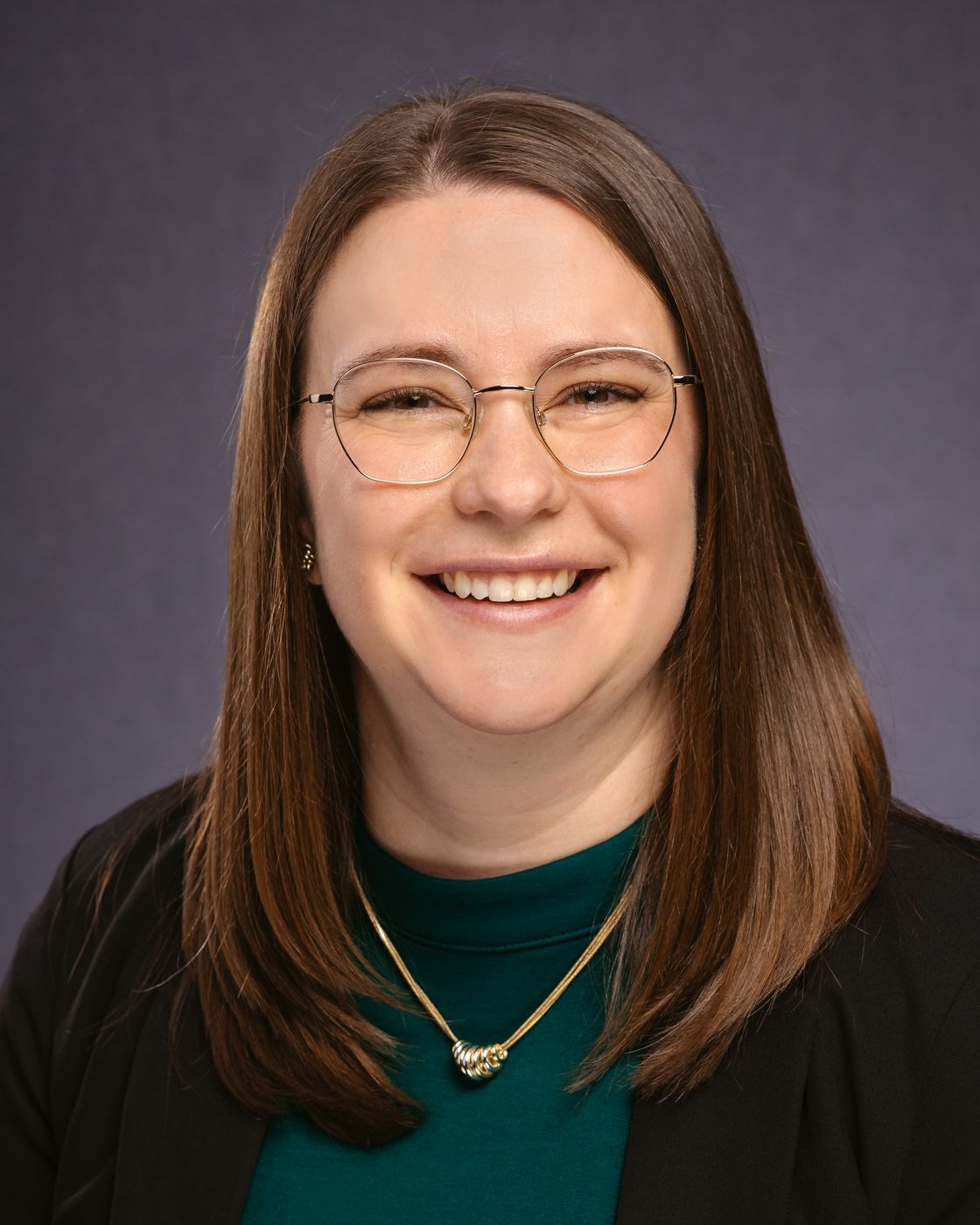 A woman wearing glasses and a necklace is smiling for the camera.