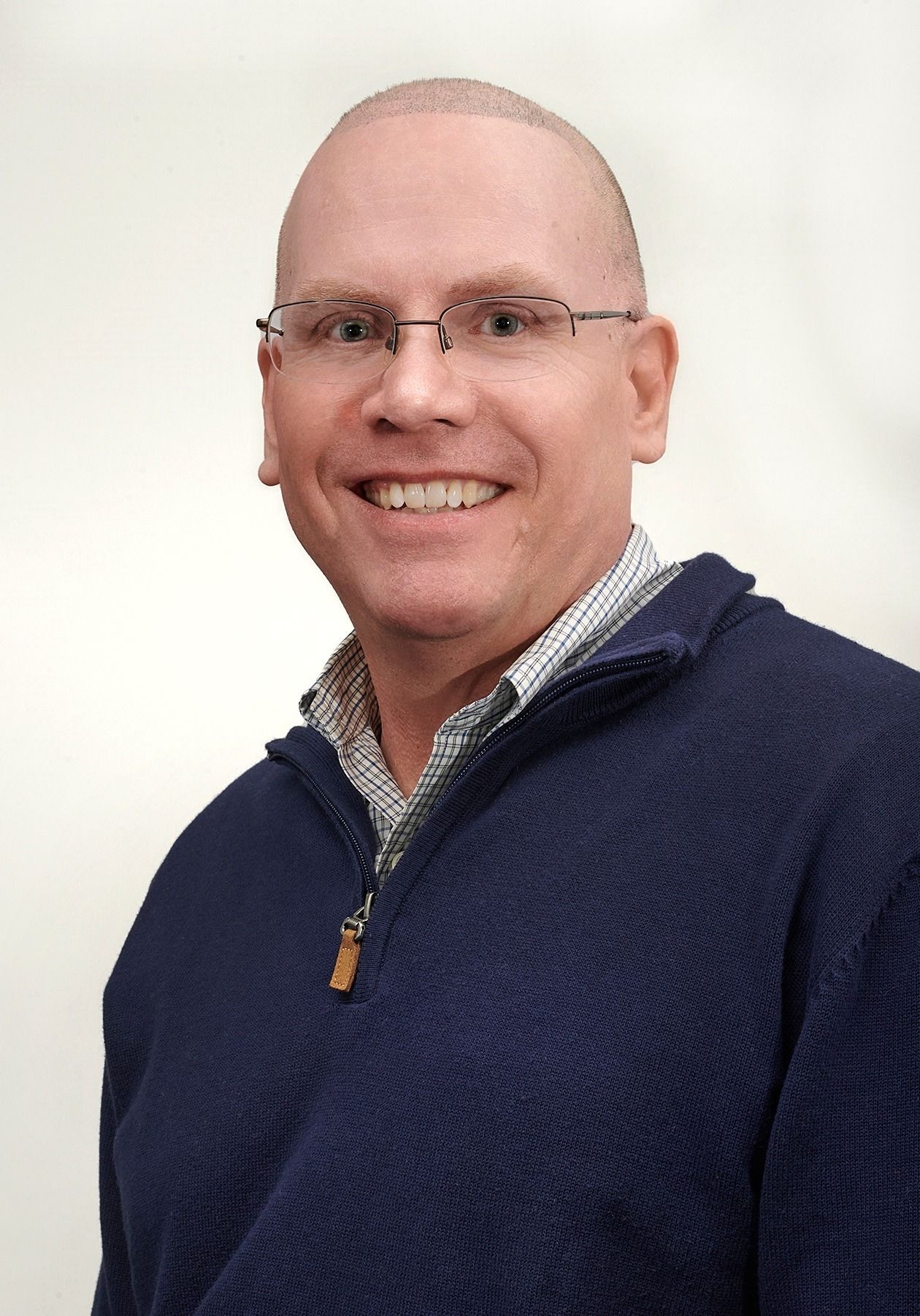 A bald man with glasses and a beard is smiling for the camera.