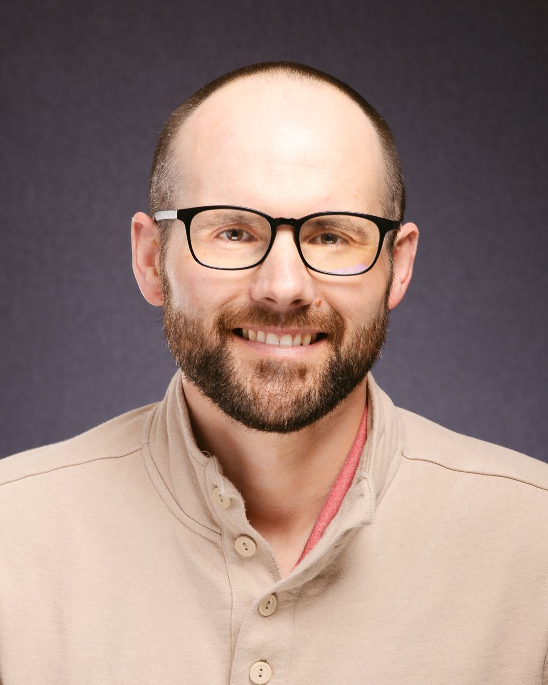 A man with glasses and a beard is smiling for the camera