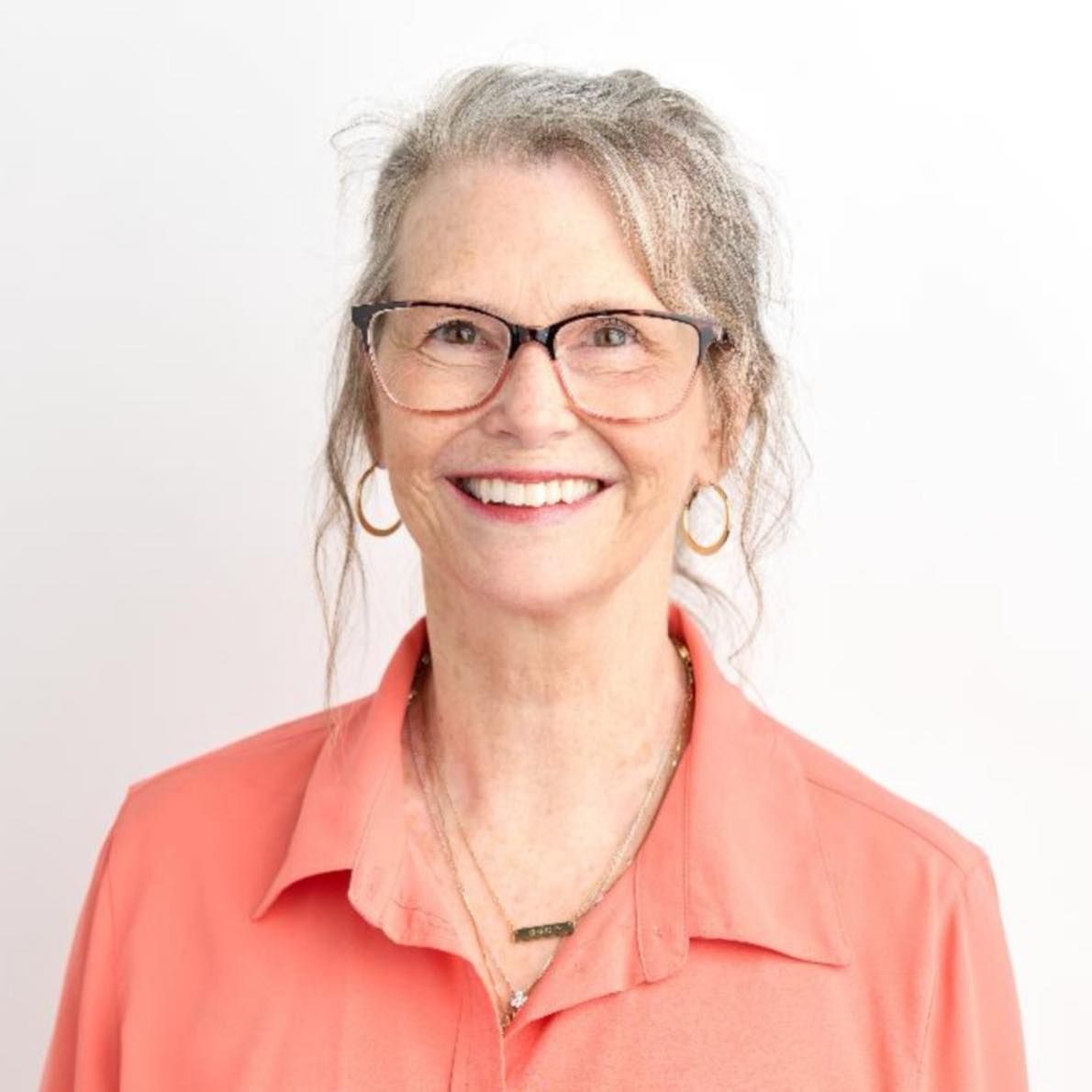 A bald man wearing glasses and a blue shirt is sitting in a chair.