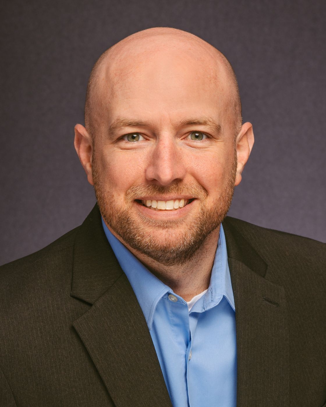 A bald man in a suit and blue shirt is smiling for the camera.