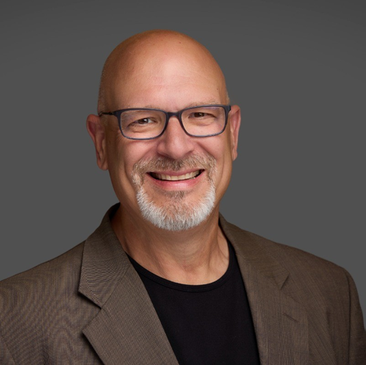 A bald man with glasses and a beard smiles for the camera