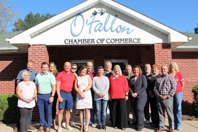 A group of people are posing for a picture in front of a chamber of commerce building.