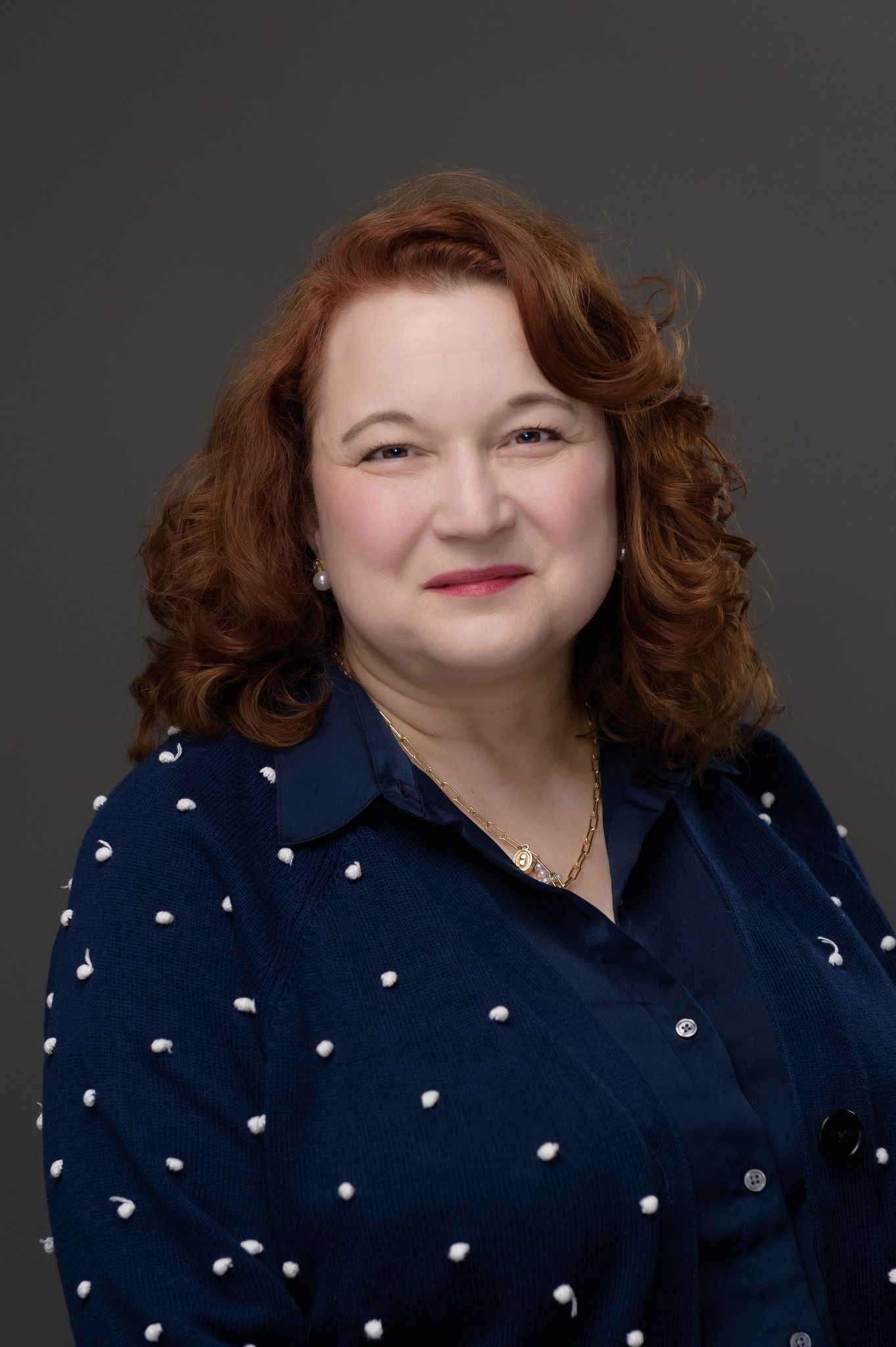 A woman in a black jacket and pink shirt is smiling for the camera.