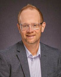 A man in a suit and glasses is smiling for the camera.