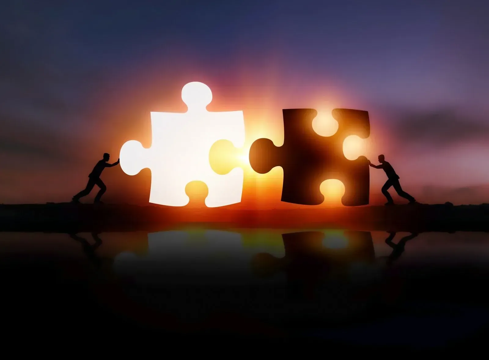 Two people are pushing puzzle pieces together at sunset