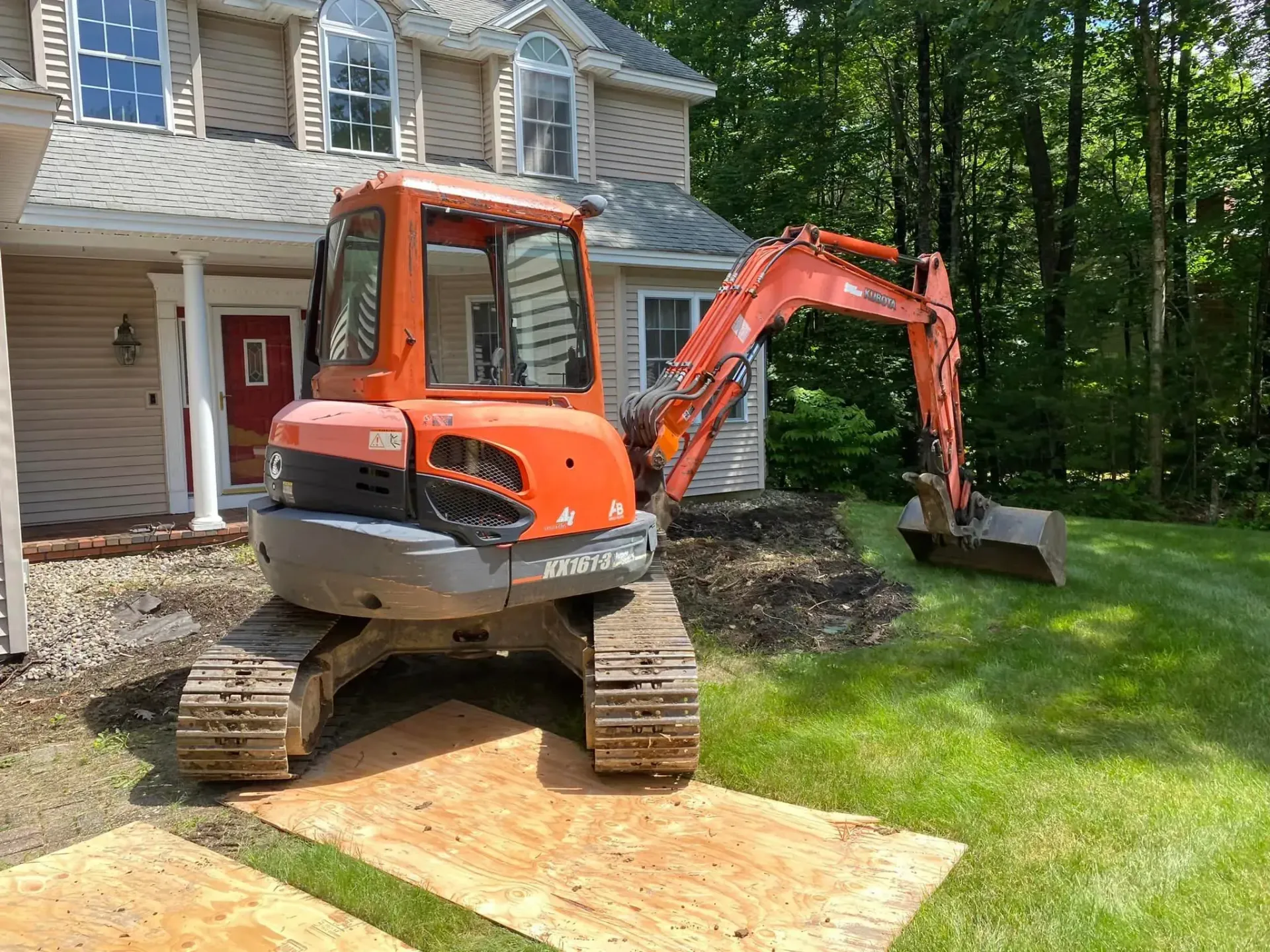 An orange excavator is parked in front of a house.